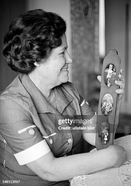 People, elder woman sits at the table and looks at a picture frame with images of her grandchildren and relations, memories, aged 60 to 70 years,...