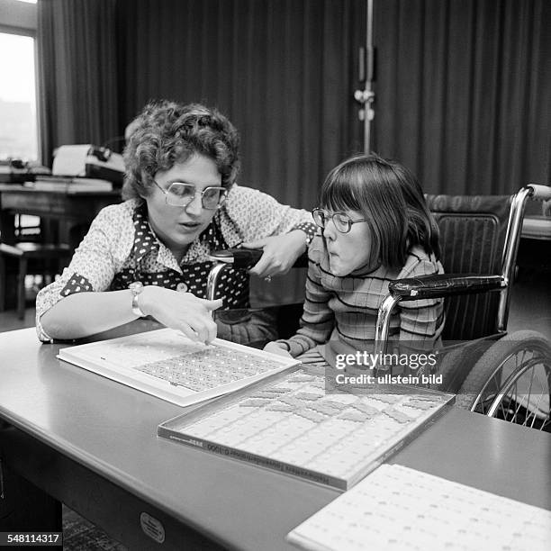 People, physical handicap, school lessons, teacher assists a girl sitting in a wheel-chair in the exercises, aged 30 to 40 years, aged 8 to 12 years,...