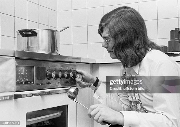 People, amateur cook, young man crouches with a ladle in front of the cooking stove and regulates the cooking temperature, a cooking pot stands on...