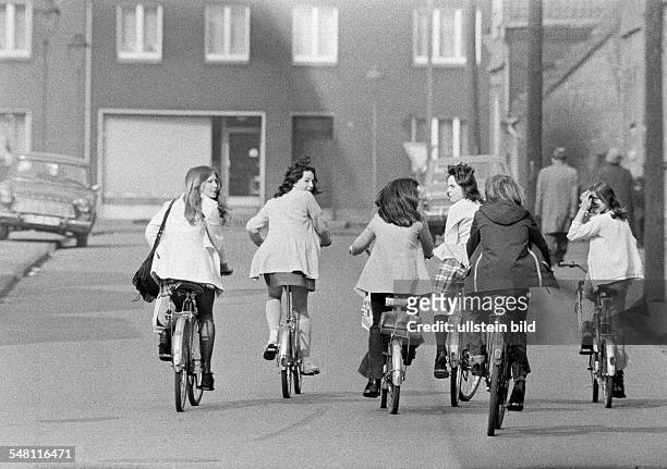 People, six young girls on bicycles drive side by on a traffic road, pleasure trip, excursion, aged 13 to 16 years -