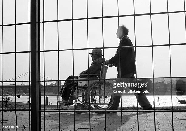 People, physical handicap, aid, older man in a wheel-chair will be pushed by a younger man, view through a lattice fence, aged 70 to 80 years, aged...