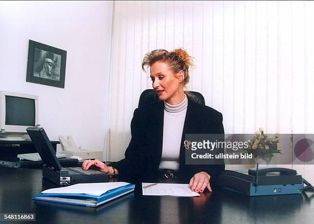 Frau sitzt im Büro hinter dem Schreibtisch und arbeitet an einem Laptop - 1996