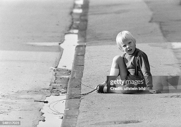 People, children, little boy sits on a pavement and plays with a stick in a puddle, aged 3 to 5 years -