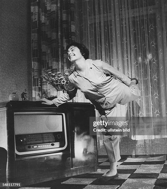 Junge Frau im Schlafanzug bei der Gymnastik auf eine Radiotruhe gestützt - 1959