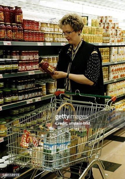 Frau beim Einkaufen in einem Supermarkt: steht vor dem Regal mit den Konserven, in ihrem Einkaufswagen liegen verschiedene Waren - 1997