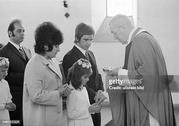 Religion, Christianity, First Communion, Eucharistic mass, in the presence of father and mother a priest administers the Holy Communion to a girl,...