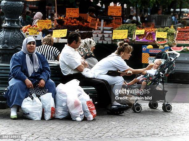 Türkische Frau mit Kopftuch und vielen Einkaufstüten ruht sich mit anderen Passanten auf der Fussgängerzone Wilmersdorfer Strasse vom...