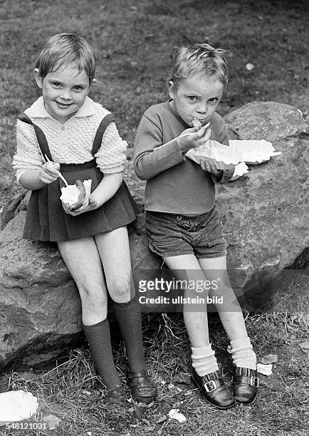 People, children, little girl and little boy sit side by side on a rock and eat fastfood, sausage and potato salad, aged 4 to 7 years -