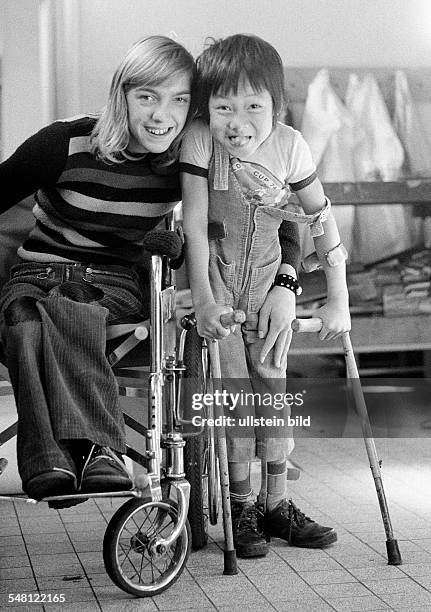 People, physical handicap, girl in a wheel-chair and boy from Vietnam with crutches posing, boy sticks out the tongue, aged 11 to 14 years, aged 6 to...