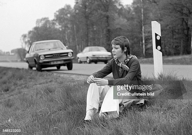 People, young woman sitting at the roadside of a country road, rest period, in the background her parking car, pulli, trousers, aged 25 to 30 years,...