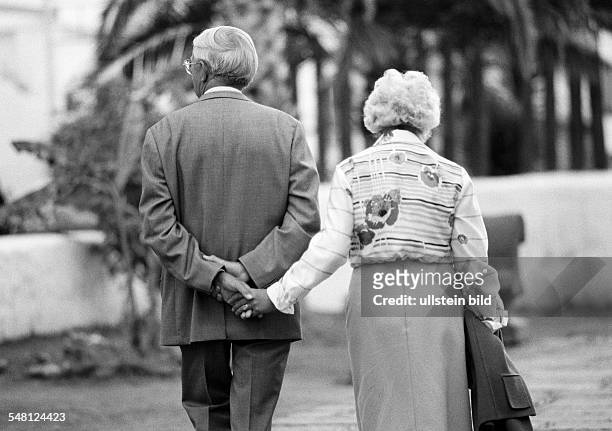 People, elder people, older couple walking hand in hand, holding hands, suit, blouse, skirt, aged 65 to 75 years, Spain, Canary Islands, Canaries,...