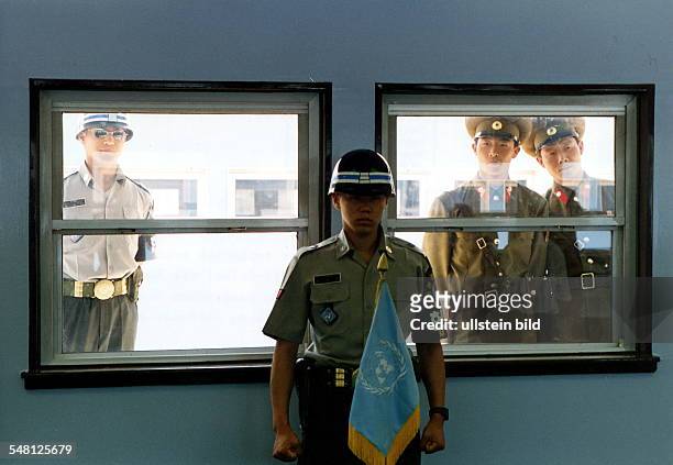 Soldier guarding the shack where South and North Koreans meet for occasional talks; a South Korean and two North Korean soldiers are looking through...