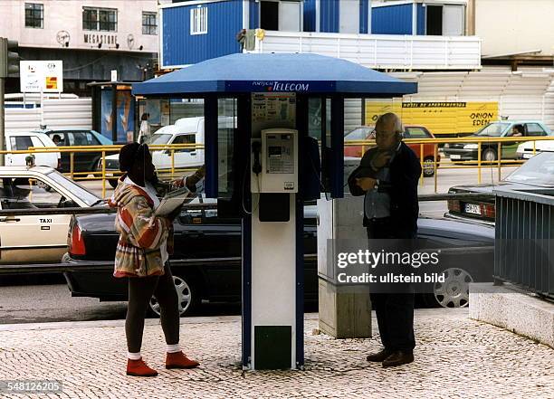 Eine Frau und ein Mann telefonieren an einer halboffenen, öffentlichen Fernsprechanlage der 'Portugal Telecom' in Lissabon - November 1997