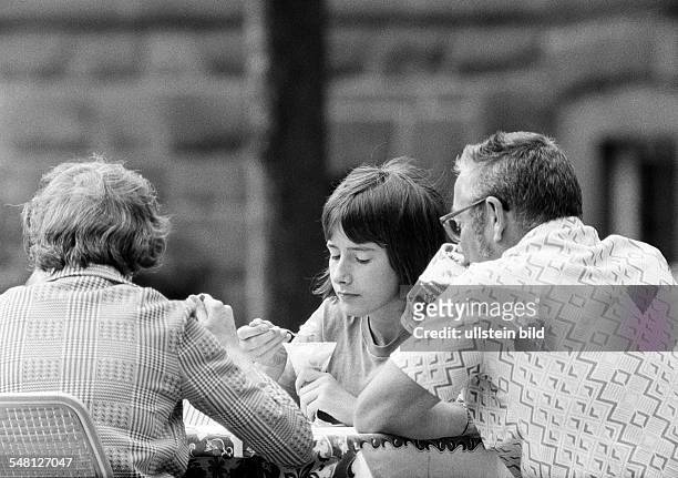 People, bored young girl and her parents sit in a beer garden nibbling ice cream, father drinks a beer, girl, aged 14 to 16 years, father, aged 40 to...