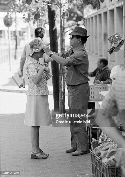 Holidays, tourism, souvenir shop, older couple, trying on of a hat, man puts on a sun bonnet to his woman, aged 60 to 70 years, Spain, Balearic...