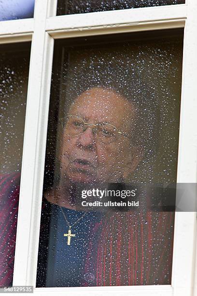 Elderly woman is looking out of the window at a rainy day -