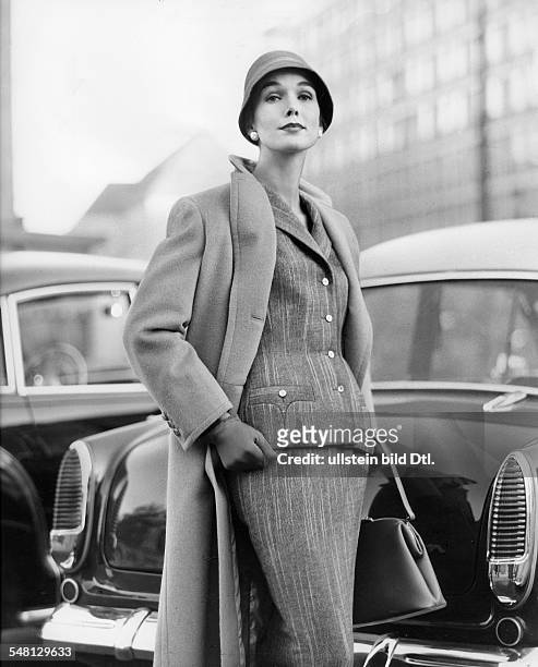 Woman wearing a tweed costume comprising a fitted jacket and narrow skirt, as well as a camel hair coat and narrow felt hat; model 'Chic' and coat...