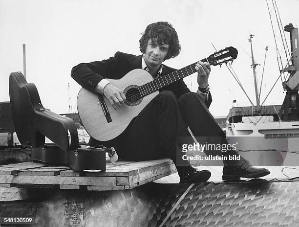 Horton, Peter *- Musiker, Autor, Oesterreich - Ganzkoerperaufnahme, sitzt Gitarre spielend an einem Hafen - undatiert