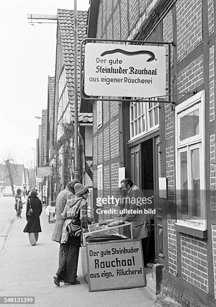People, shopping, tourists stand at a stall offering smoked eel from the Steinhude Lake named Steinhuder Meer, row of houses, half-timbered houses,...