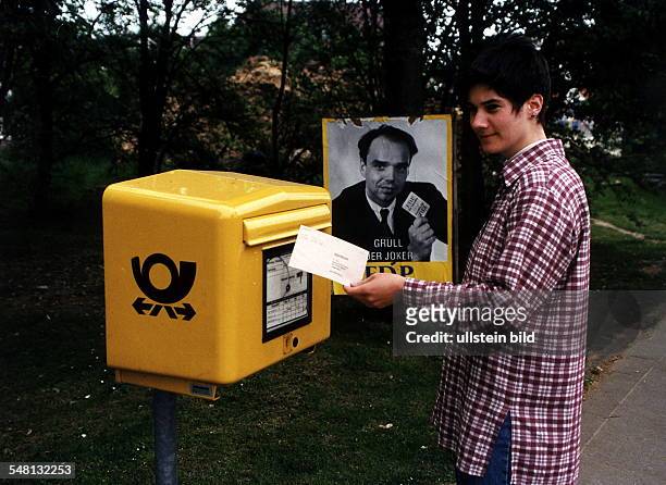 Symbolbild Briefwahl: eine Wählerin steckt einen Briefwahlumschlag in einen Breifkasten; dahinter ein Wahlplakat der FDP - 1995