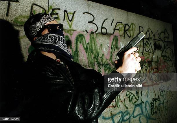 Ein Mitglied der Jugendgang '36 Boys' posiert mit einer Gaspistole vor einer mit Graffiti beschmierten Wand - 1996