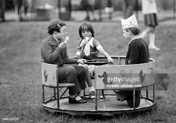 People, children, childrens treat, two girls and a boy with a paper cap on his head sit in a roundabout and lick ice cream, aged 5 to 8 years -