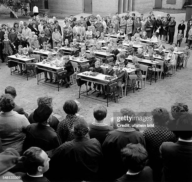 Einschulungsfeier im Freien: Kinder auf Schulbänken im Kreis der Eltern - 1970