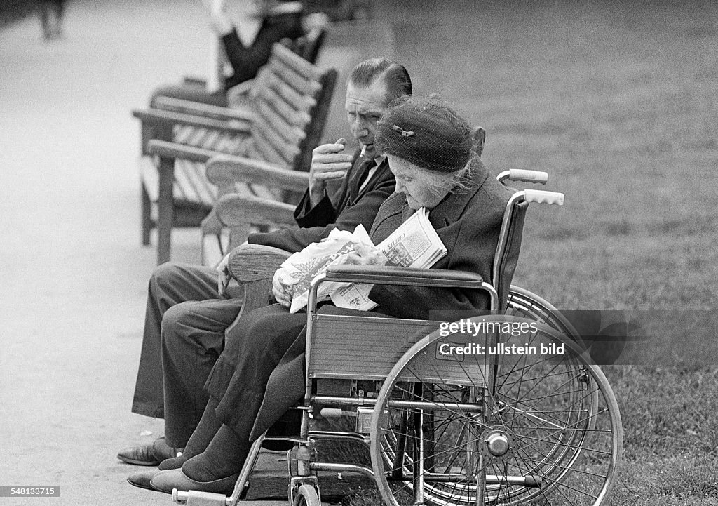 People, physical handicap, older woman sits in a wheel-chair, her husband sits beside her on a bench, aged 65 to 75 years, Great Britain, England, London - 02.06.1979