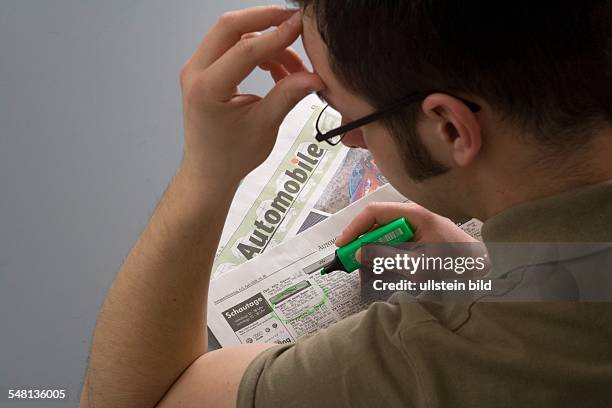 Young man reading second-hand car offers in a newspaper -
