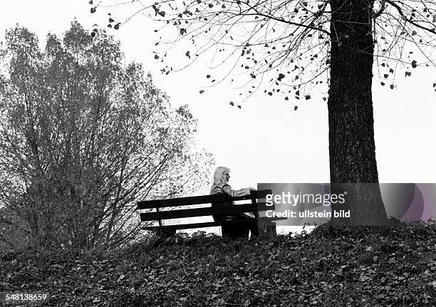 Symbolic, loneliness, young woman sitting on a bench under a tree, autumnal, backlight, silhouette, aged 25 to 35 years, Elisabeth -