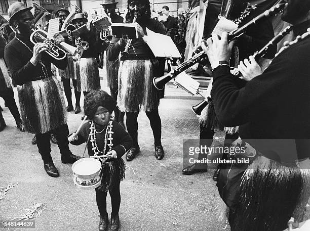 Federal Republic of Germany Bavaria Munich: Scenes from the Munich Carnival - small boy in a grass skirt and with drums standing amidst a brass band...