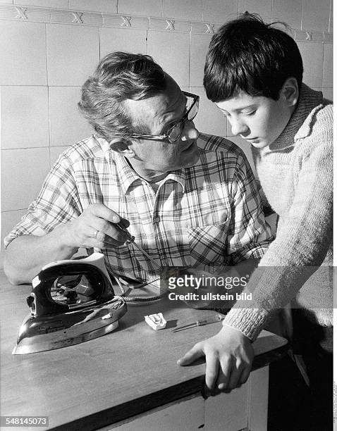 Vater und Sohn reparieren den Stecker des Bügeleisens - undatiert März 1967 Fotografie: Hugo Schmidt-Luchs