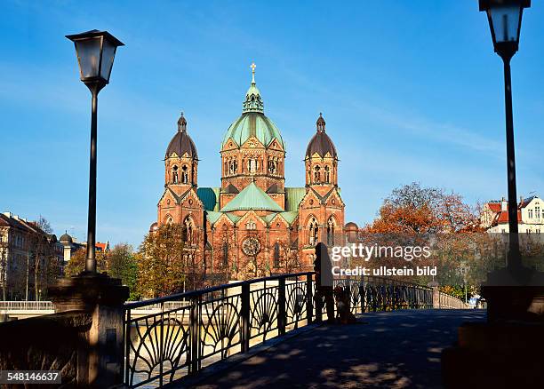 Germany Bavaria Munich - Silhouette of a Woman with dog standing on Footbridge acoross the river Isar with St. Lucas Church in the background.