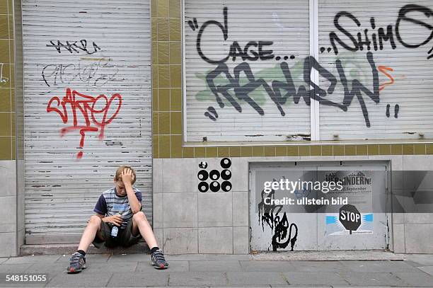 Sad boy with beer bottle in front of a closed shop with graffity -