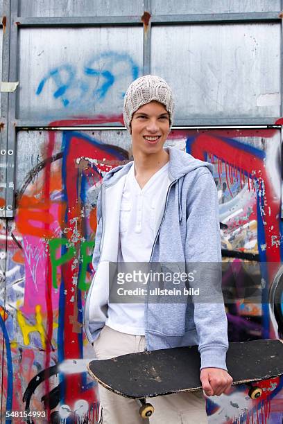 Young man wearing a sweater with hood in front of a wall with graffity with skate board - 2010
