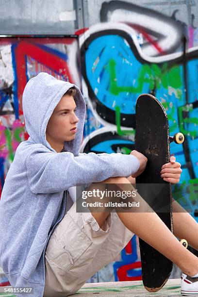 Young man wearing a sweater with hood in front of a wall with graffity with skate board - 2010