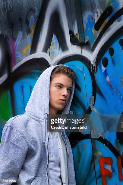 Young man wearing a sweater with hood in front of a wall with graffity - 2010
