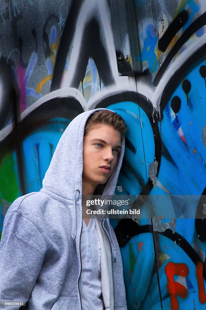 Young man wearing a sweater with hood in front of a wall with graffity - 2010