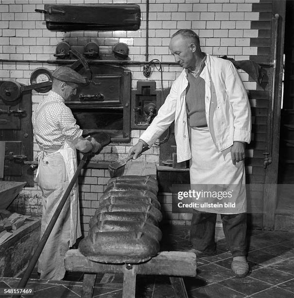 Bäcker mit Gehilfe vor dem Backofen: beim Entmehlen frisch gebackener Brote - 1960