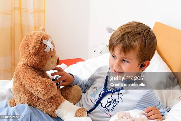Sick boy in bed is examining his teddy bear with a stethoscope -