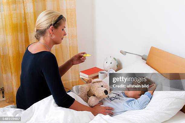 Sick boy in bed, mother is takng his temperature -