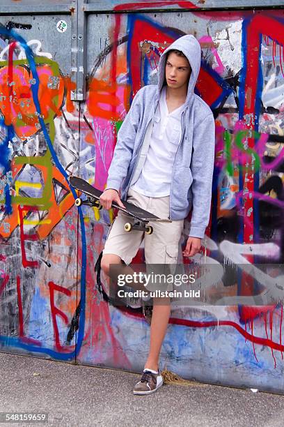 Young man wearing a sweater with hood in front of a wall with graffity with skate board - 2010