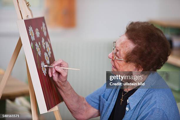 Elderly woman is painting a picture -