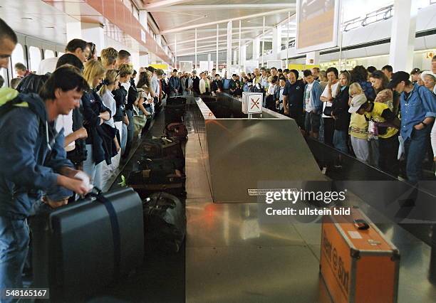 Reisende warten am Förderband der Gepäckausgabe auf ihr Gepäck - Mai 2000