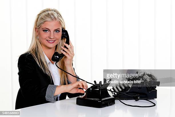 Woman making a phone call with an old telephone, on the desk an old typewriter -