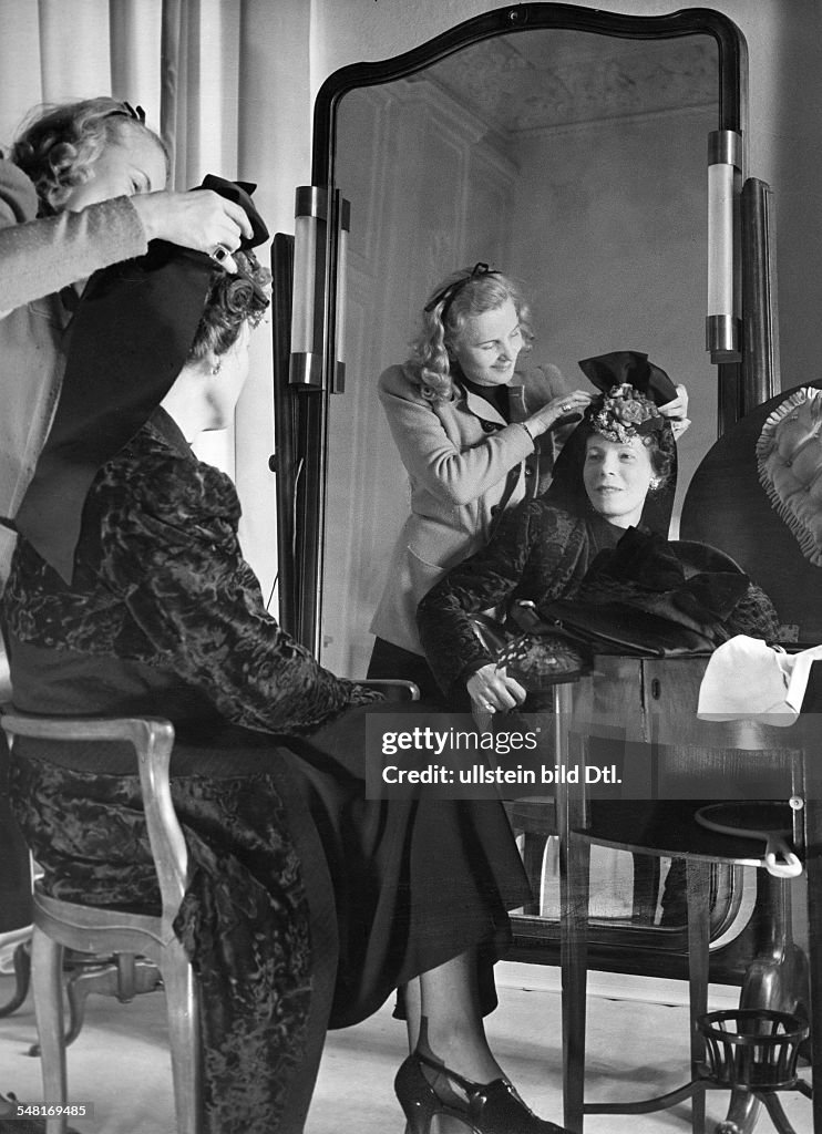Mrs von Wülfing trying on a hat in the salon of Berlin modiste and hatter Madame Berthe - 1941 - Photographer: Regine Relang - Published by: 'Die Dame' 13/1941 Vintage property of ullstein bild