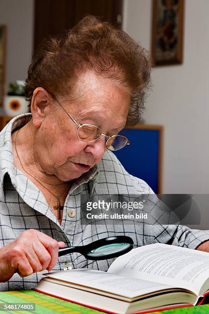 Elderly woman with glasses is reading a book with a lense -