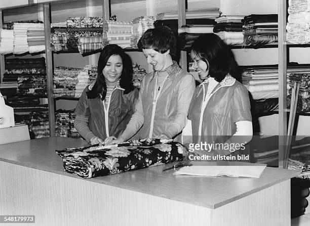 Stoffgeschäft in Potsdam: junge Vietnamesinnen in der Ausbildung mit einer Verkäuferin vor Stoffballen - 1983