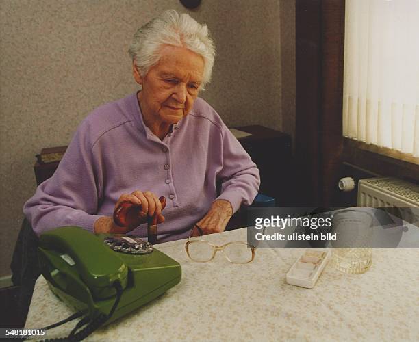 Alte Frau sitzt am Tisch und wartet auf einen Anruf - 1995