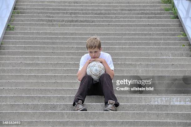 Lonesome boy with football sitting on the stairs -